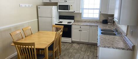 Una cocina con armarios blancos, una mesa de comedor de madera y sillas.