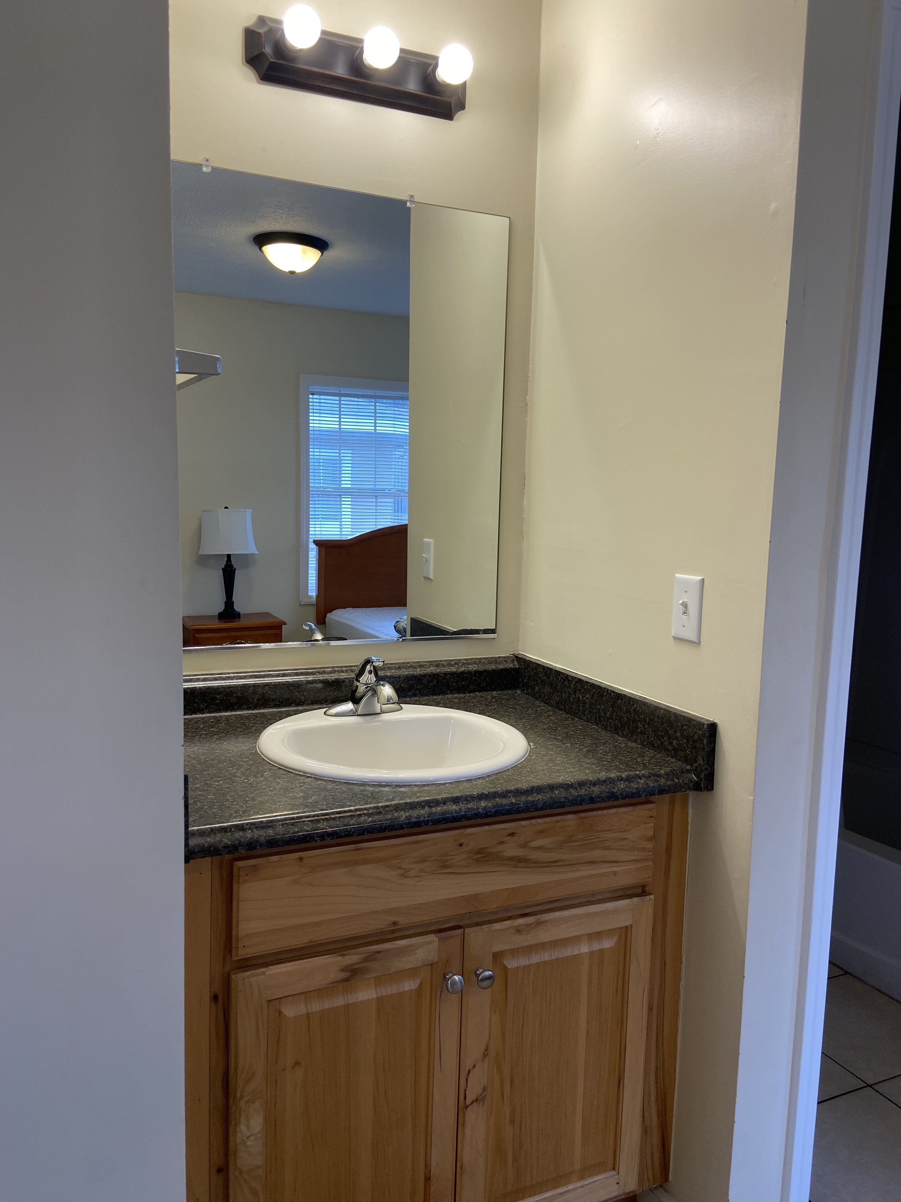 A bathroom with a white sink, wooden cabinets, a mirror, and a light fixture above the mirror.