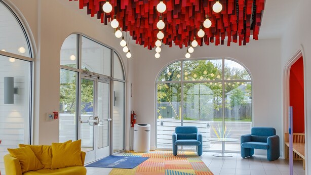 Un interior moderno con una alfombra geométrica colorida, un sofá amarillo y adornos colgantes rojos.