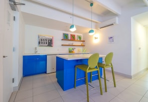 Une cuisine moderne avec des meubles bleus, un plan de travail blanc et un coin bar agrémenté de deux chaises vertes.