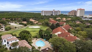 Un complexe hôtelier doté d’une piscine, d’un parcours de golf et d’hôtels situés en bord de mer, visibles en arrière-plan.
