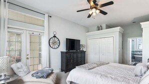 Une chambre à coucher comprenant un lit, une chaise, un téléviseur, une armoire et un ventilateur de plafond.