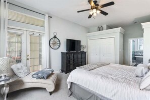 Una camera da letto con un letto, una sedia, una televisione, un armadio e una ventola a soffitto.