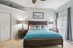 Une chambre à coucher avec un lit en bois, deux tables de chevet avec des lampes, un tableau accroché au mur, une porte et une fenêtre avec des rideaux.