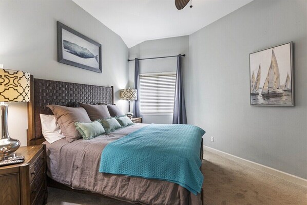 A bedroom with a bed, a nightstand, a lamp, a window with curtains, and wall art.