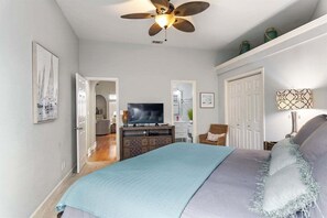 A bedroom with a bed, a ceiling fan, a television, and a dresser.