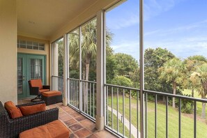 Un balcón con mobiliario de mimbre y vistas a un jardín cuidado.