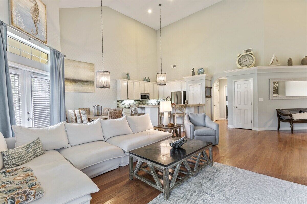 Een ruime woonkamer met een witte bank, een salontafel en een grijze fauteuil. Er is een keuken met witte kasten en een eettafel.