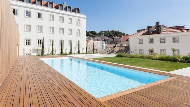 Ein Schwimmbad mit Holzterrasse, umgeben von Gebäuden mit roten Ziegeldächern und weißen Fassaden.