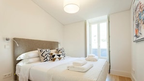 Ein ordentlich gemachtes Bett mit weißen Leinen und einer gesteppten Decke, einem Kopfteil und einem Fenster mit Ausblick.