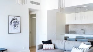 Ein modernes Wohnzimmer mit grauem Sofa, einem gerahmten Kunstwerk an der Wand und einer Küche im Hintergrund.