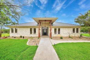 A two-story stone house with a central entrance, a covered porch, and a well-maintained lawn. - Luxury Ranch Retreat Pool, Sleeps 18 (Dripping Springs)