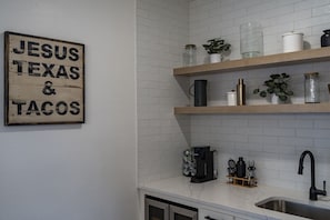 A kitchen with white tiled walls, wooden shelves, and a coffee maker. - Luxury Ranch Retreat Pool, Sleeps 18 (Dripping Springs)