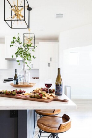 A modern kitchen with a central island, bar stools, a wine bottle, and a glass of red wine. - Luxury Ranch Retreat Pool, Sleeps 18 (Dripping Springs)