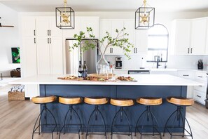 A modern kitchen with a central island, bar stools, white cabinets, and pendant lighting.