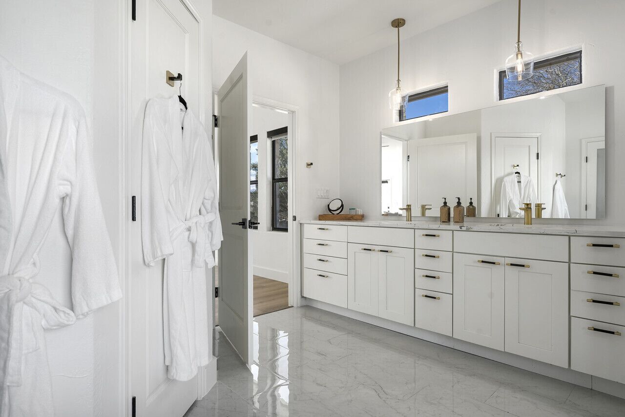 Un baño moderno con un espejo grande, armarios blancos y ducha a pie.