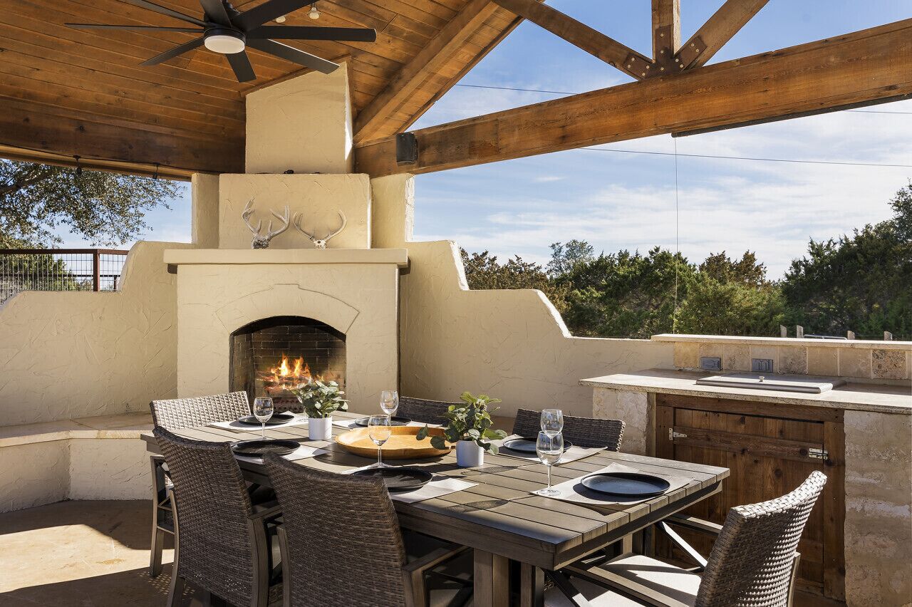 An outdoor patio with a built-in grill and fireplace, surrounded by wicker furniture and potted plants.