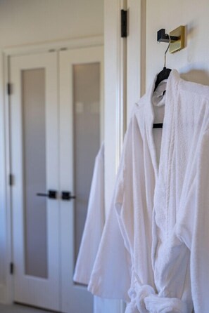 A white robe hanging on a hook in a room with white doors and a light switch on the wall. - Luxury Ranch Retreat Pool, Sleeps 18 (Dripping Springs)