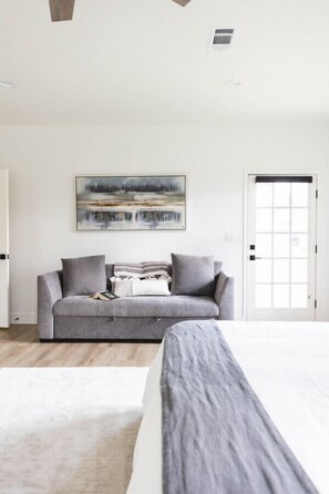 A bedroom with a bed, a grey sofa, a painting, and a door. - Luxury Ranch Retreat Pool, Sleeps 18 (Dripping Springs)
