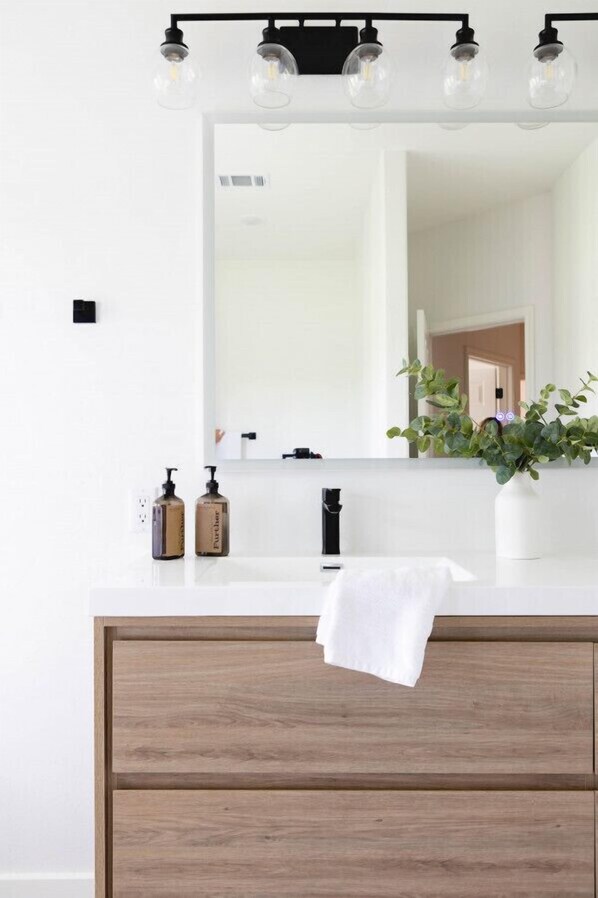 A bathroom with a white vanity, a mirror with lights, a towel, and a plant.