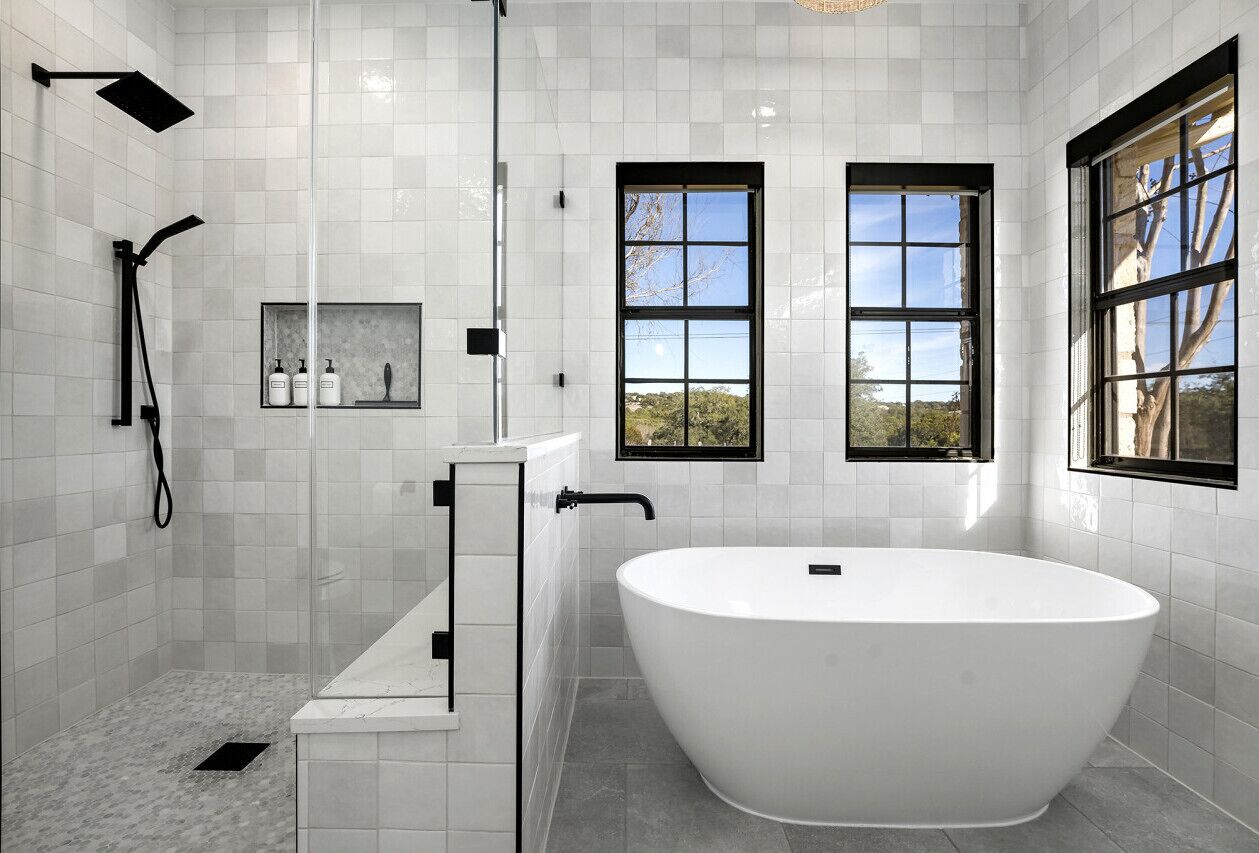 Un baño moderno con una bañera independiente, ducha con cerramiento de vidrio y dos ventanas que dejan entrar luz natural.