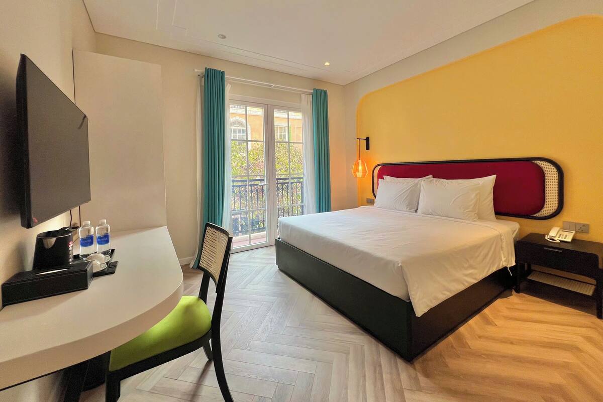 Una habitación de hotel con una cama, un escritorio con una silla, un televisor y un teléfono en una mesita de noche.