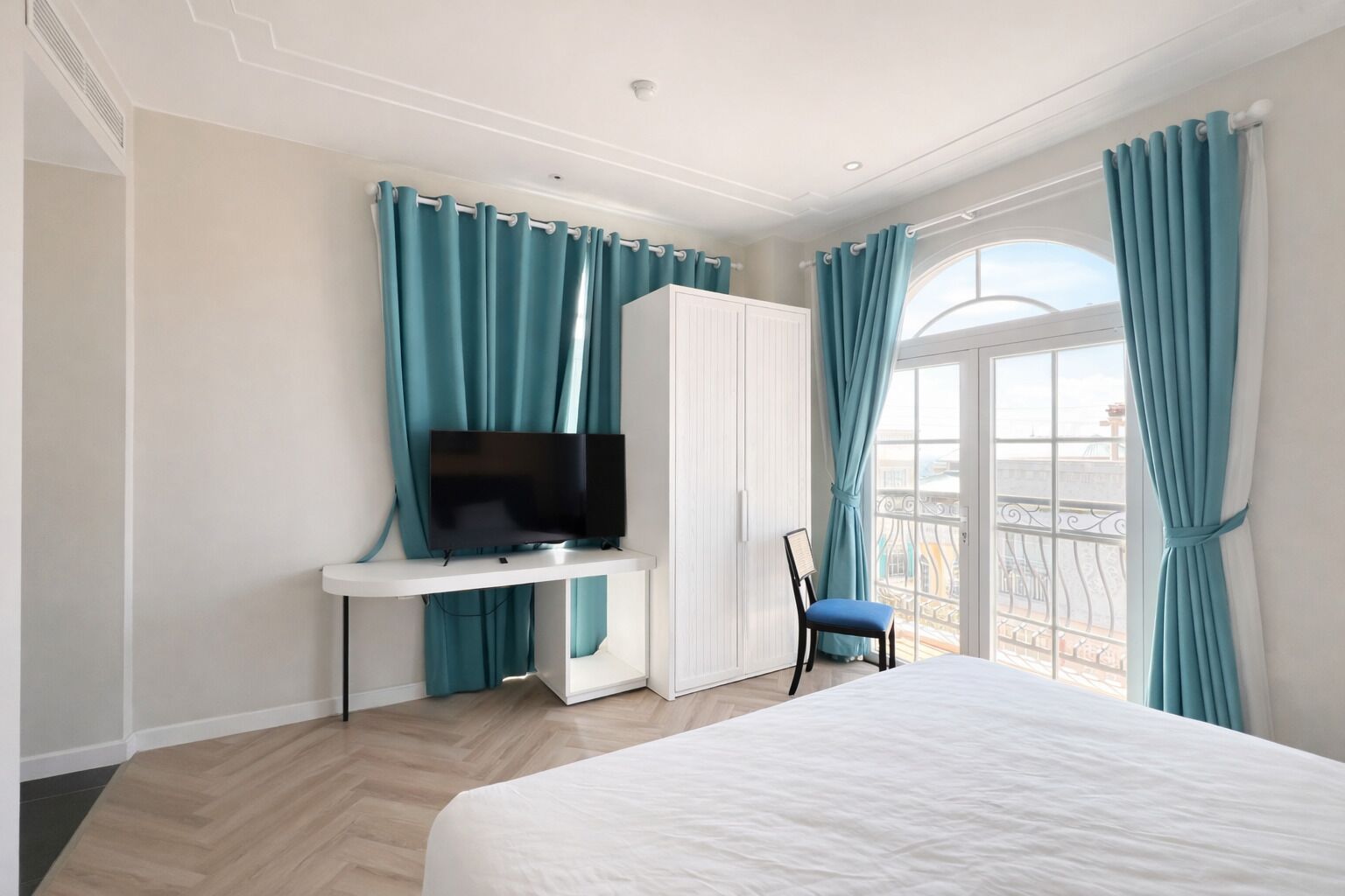 Ein Hotelzimmer mit einem Bett, einem Fernseher auf einem weißen Standfuß, einem Schreibtisch und einem Sessel.