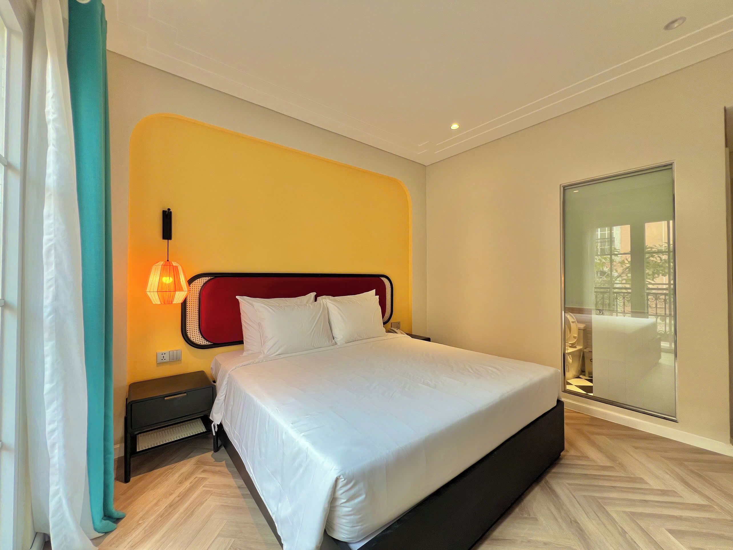 A hotel room with a bed, a nightstand, a lamp, a window with a view, and a door.
