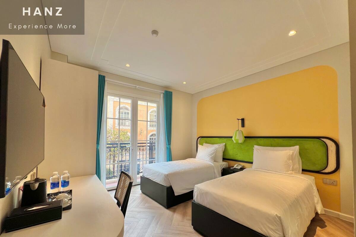 Habitación de hotel con dos camas, un escritorio con silla, cafetera y ventana con cortinas.