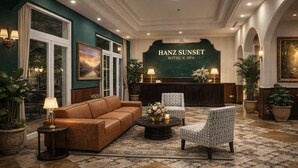 Eine Lobby mit einer braunen Ledersofa, gemusterten Sessel, einem Couchtisch und einem Empfangstresen mit dem Schild "HANZ SUNSET HOTEL & SPA".