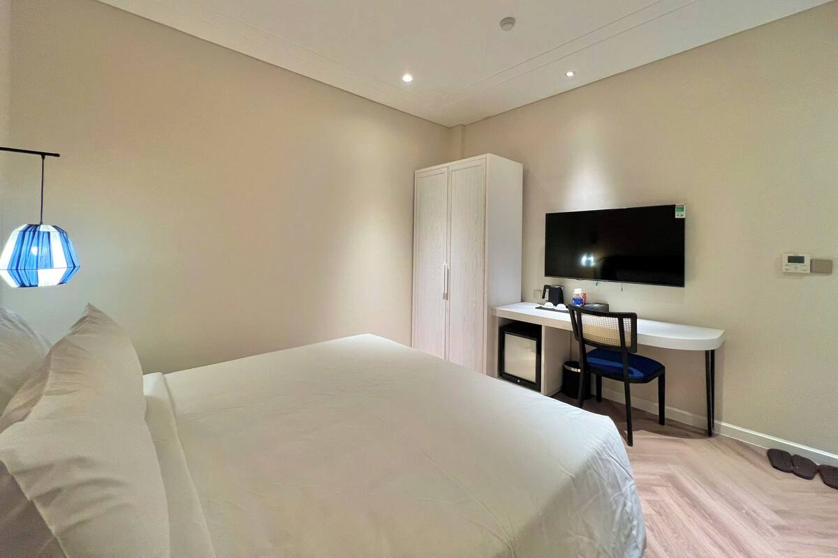 Una habitación de hotel con cama, escritorio, silla, televisor y armario.