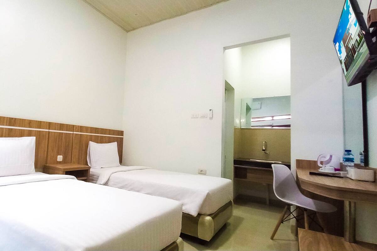 A hotel room with two single beds, a wooden headboard, a desk with a chair, a mirror, and a television.
