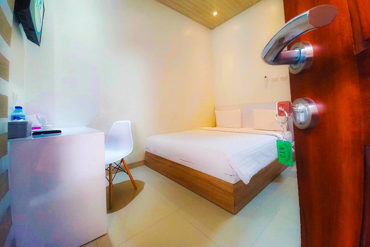 A hotel room with a bed, a desk, a chair, and a wooden door.