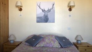 Une chambre à coucher comprenant un lit, deux tables de chevet, deux lampes fixées au mur et un tableau représentant un cerf accroché au mur.