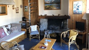Un salon chaleureux avec une cheminée, des meubles en bois et un tableau représentant un paysage accroché au mur.