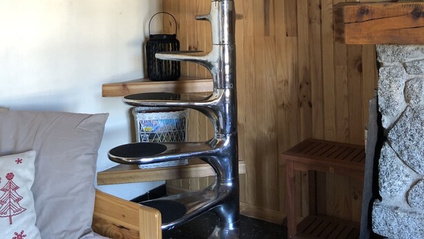 Une pièce de taille modeste avec un mur en bois, une étagère en métal, un petit tabouret en bois, un banc rembourré et une lampe fixée au mur.