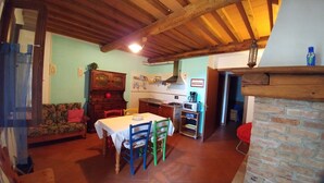 A cozy kitchen with wooden beams, a dining area with a table and chairs, and a living room with a sofa. - The Barn Owl apartment in farmhouse in the countryside (Bivio Ravi)