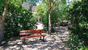 A wooden bench in a shaded park area with trees and a stone building in the background. - The Barn Owl apartment in farmhouse in the countryside (Bivio Ravi)