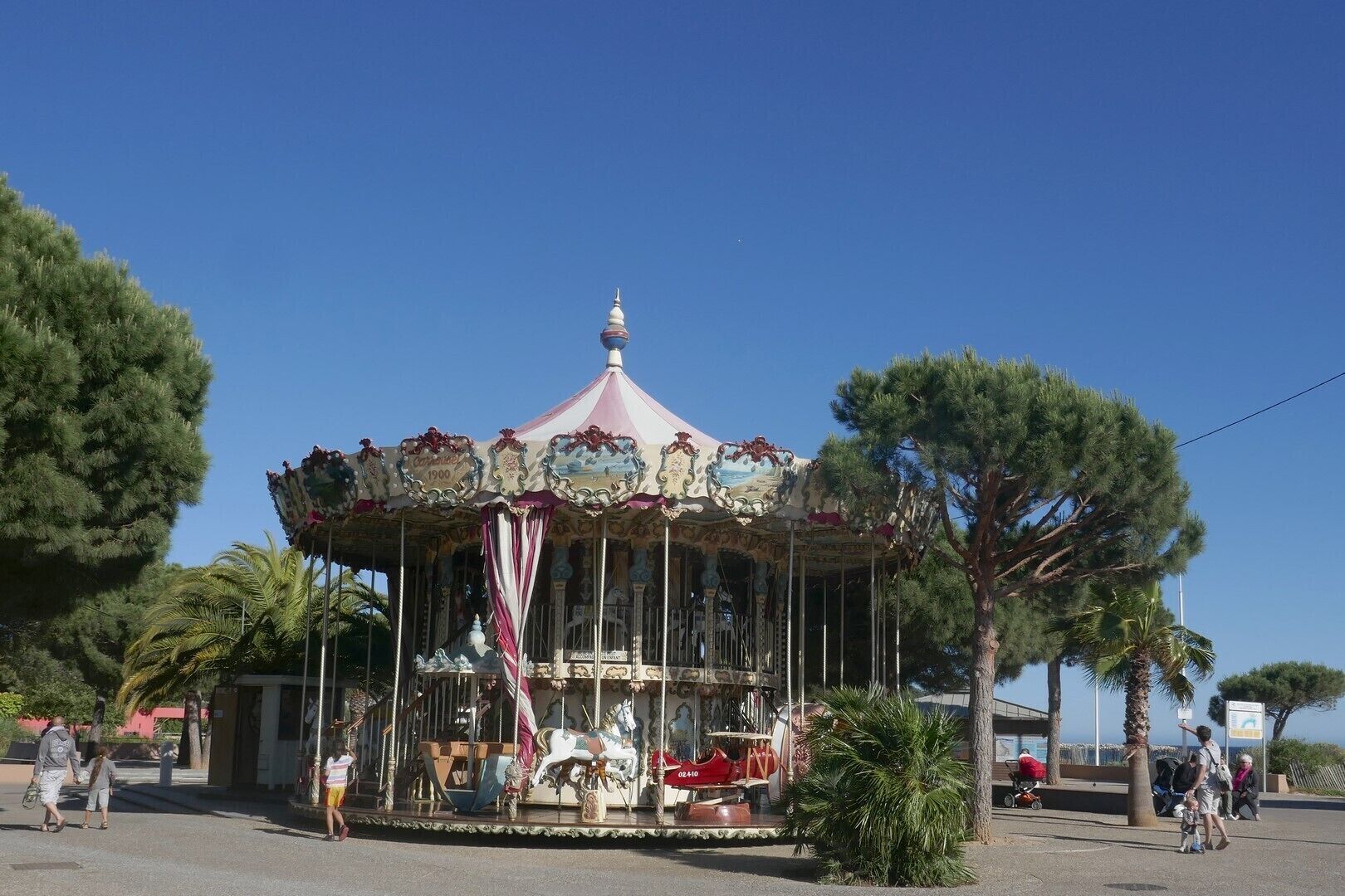 Un carrusel con decoraciones elaboradas y un diseño antiguo, rodeado de palmeras y un cielo azul despejado.