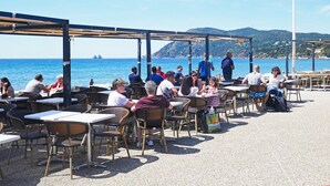 Ein Straßencafé mit Tischen und Stühlen mit Blick auf ein Gewässer und Hügel.