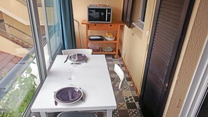 Ein kleiner Balkon mit Tisch für Zwei, einem Fernseher auf einem Schrank und einem Fenster mit Blick ins Grüne.