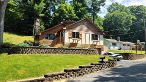 A cabin with a stone retaining wall, a porch with chairs, and a car parked in front. - The Stonefire Cabin! (Sparta Township)