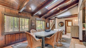 A dining area with a wooden table and wicker chairs, large windows with a forest view, and a staircase leading to another level. - Finch Haven in Homewood (Homewood)