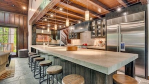 A modern kitchen with a large island, bar stools, stainless steel appliances, and a wooden ceiling. - Finch Haven in Homewood (Homewood)