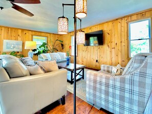 A cozy living room with wooden walls, a sofa, a plaid armchair, a coffee table, and pendant lighting.