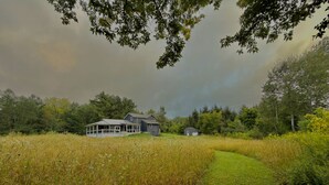 Ett hus med en inglasad veranda och en mindre byggnad på en åker med högt gräs.