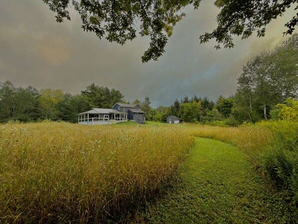 A house with a covered porch and a smaller building in a field with tall grass. - Amazing Stargazing Retreat (Naples)