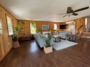 A spacious living room with a light blue sofa, a wooden coffee table, and several potted plants.