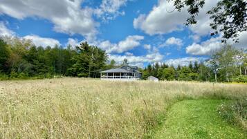 A house with a large porch, surrounded by a field and trees.