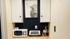 Une petite cuisine équipée d’un four à micro-ondes, d’un grille-pain et d’un petit réfrigérateur. Un tableau encadré représentant une vache est accroché au mur, au-dessus du comptoir.